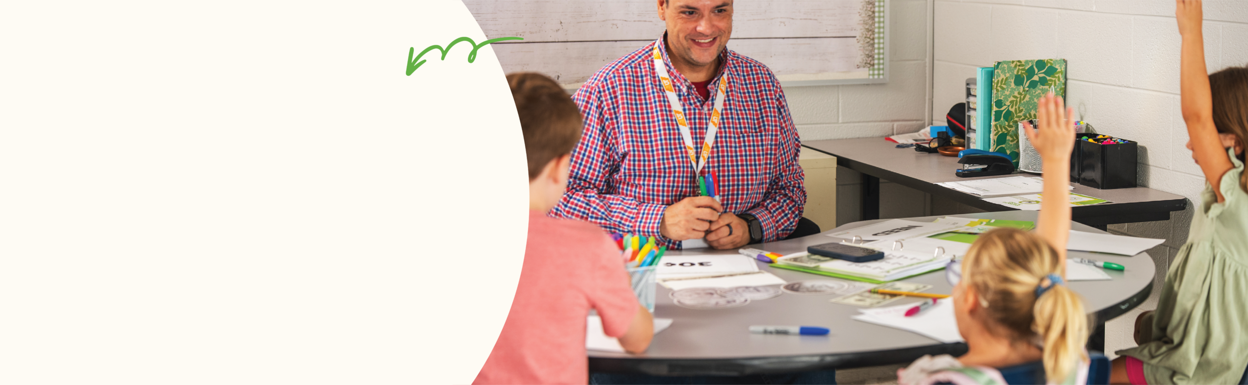 teachers smiling at round table with three kids sitting around the table raising their hands