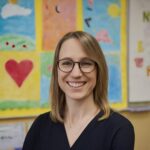 female teacher with glasses smiling at camera in a classroom